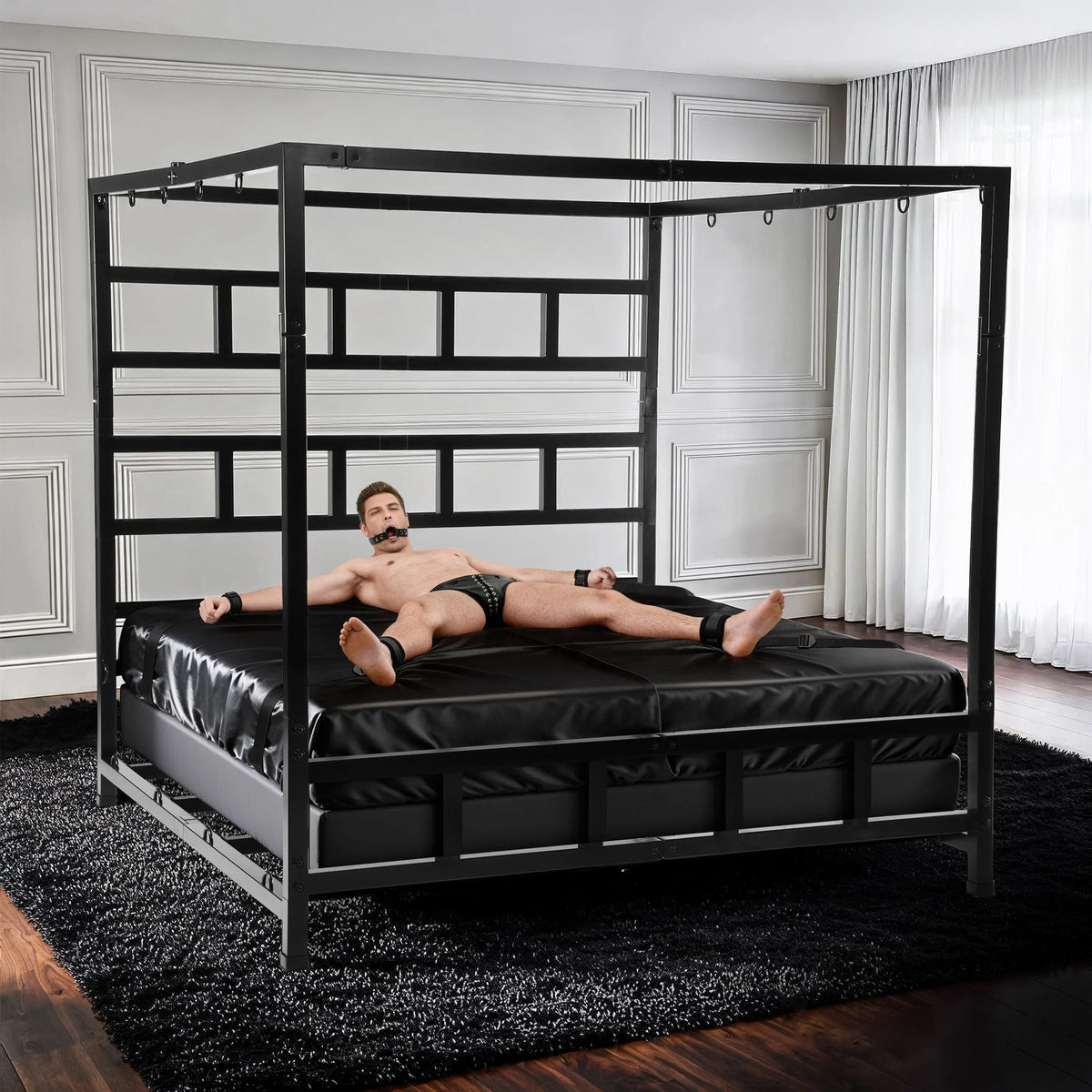 Gagged model cuffed spread-eagle to the D-rings of the King Size Bondage Bed on black sheets, Fort Troff