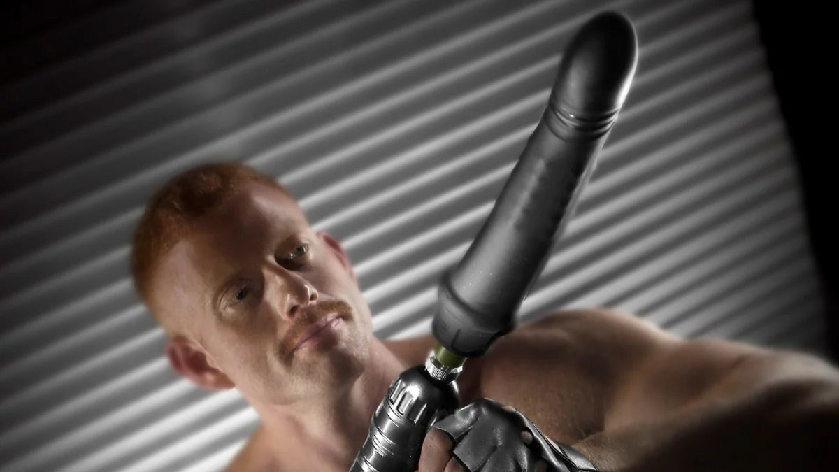 Shirtless model in fingerless gloves gripping the Gunner System handheld fucking machine, Fort Troff