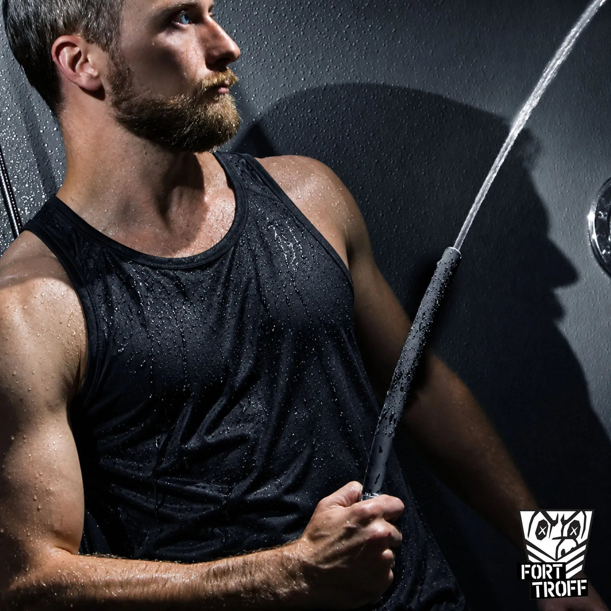 Apex Shower Set in use, bearded model in a soaked black tank top gripping the silicone nozzle as water sprays, Fort Troff