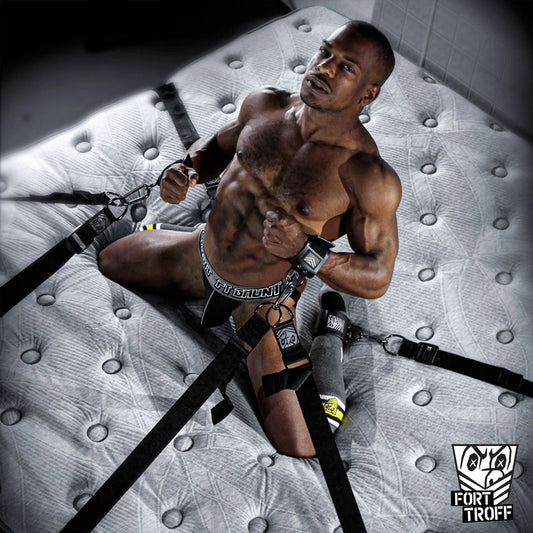 Model in a jock strapped to the Bed Bondage under-bed restraint system by his wrists and ankles, Fort Troff