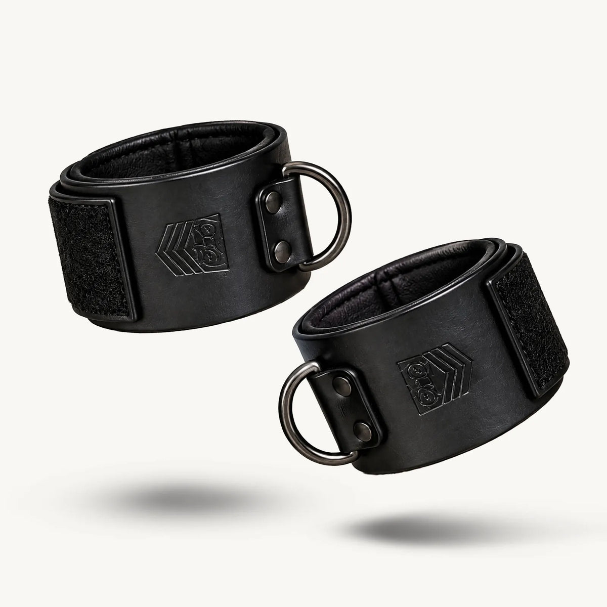 Leather Ankle Cuffs pair on white, black leather with Velcro closures and gunmetal D-rings, Fort Troff