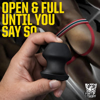 Hand holding the black Kum Keeper plug beside a model in a red jockstrap, text reads Open and Full Until You Say So, Fort Troff