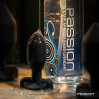 Passion Natural water-based lube coating a black silicone butt plug beside the 34 oz bottle, Fort Troff